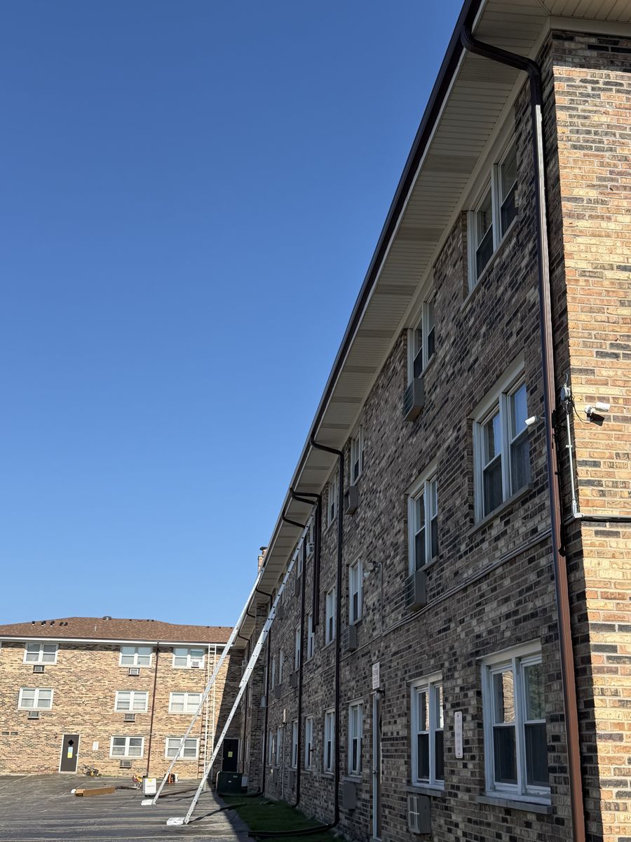 Fresh gutter and downspout run along a three-story brick apartment building with an extension ladder set against it