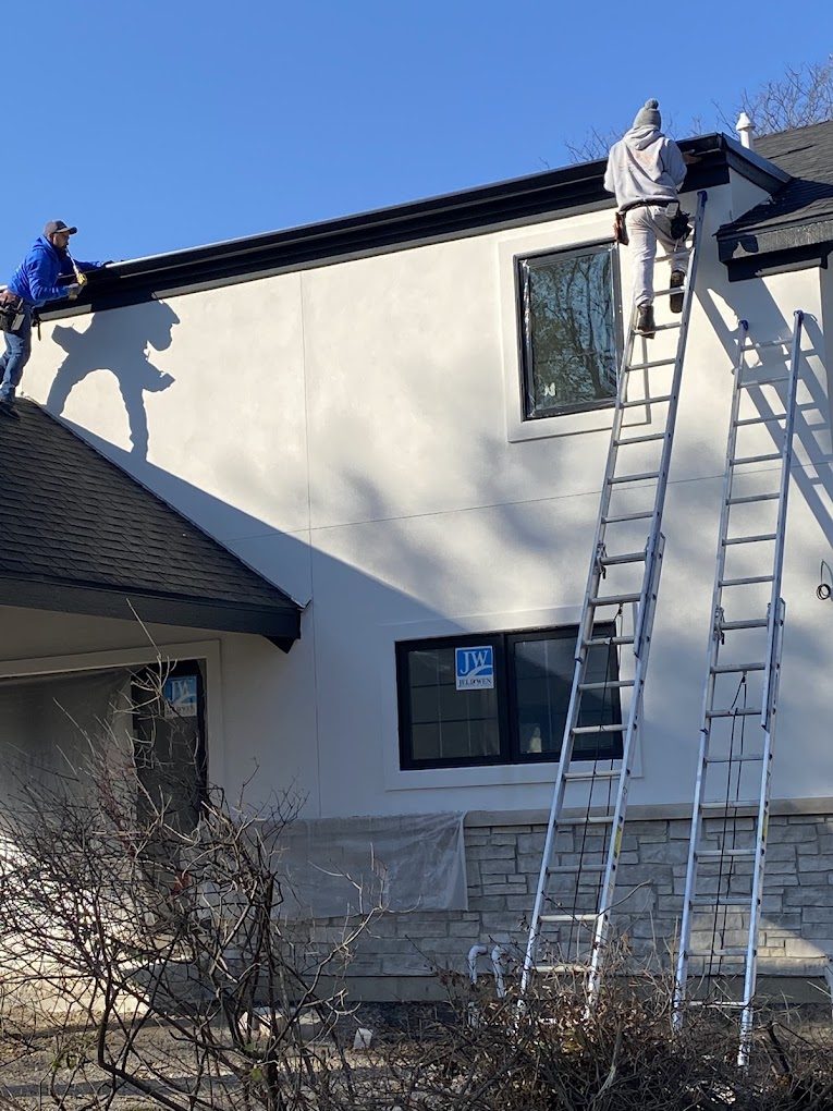 Two Family Gutters and Guards crew members on ladders setting a new gutter run along a two-story home