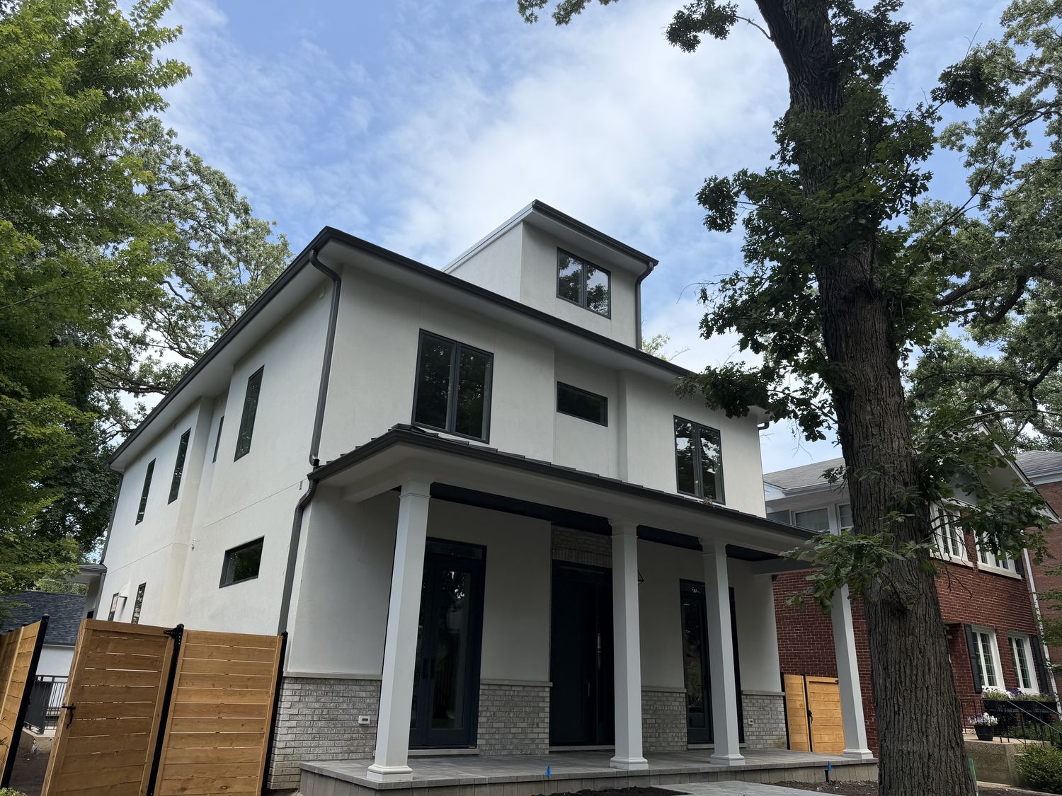 Finished white stucco new-construction home with dark seamless gutters wrapping the roofline