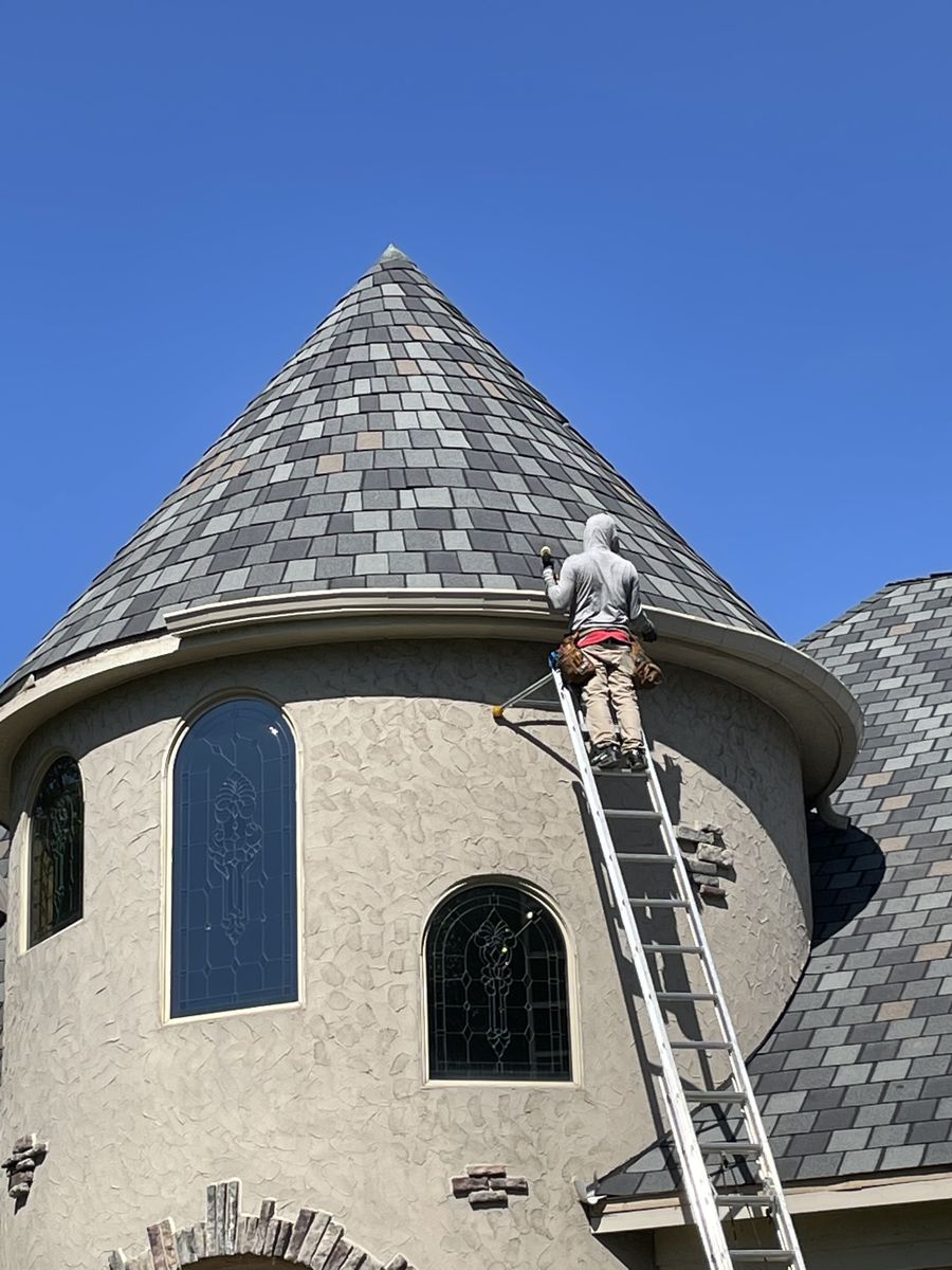 Installer up an extension ladder fitting gutter to the curved roofline of a slate-roofed turret
